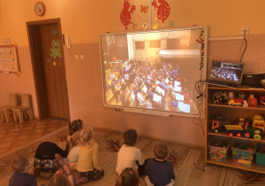Dzieci oglądają koncert muzyczny w filharmonii na tablicy multimedialnej.